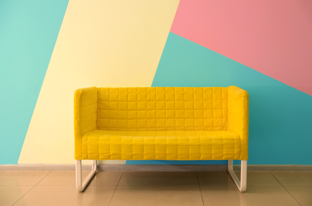 A colourful patterned wall, behind a bright yellow couch